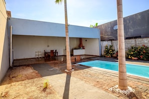 A backyard with a swimming pool, a barbecue area, and a dining set.
