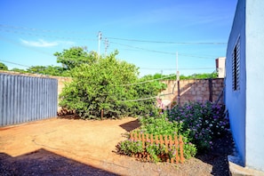 A fenced backyard with a wooden fence, a small garden with purple flowers, and a brick wall.