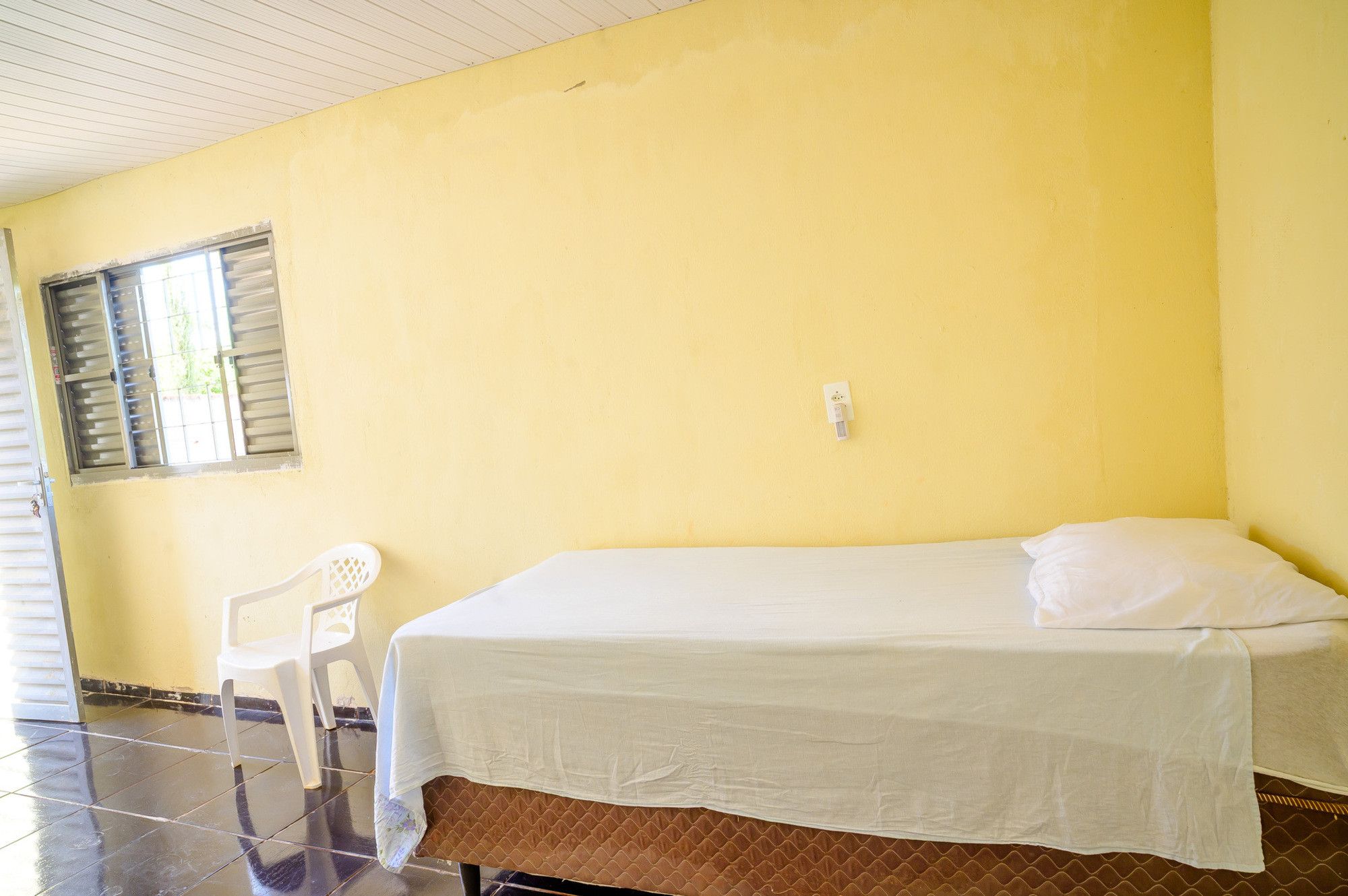 Una habitación con cama, una silla y ventana con persianas.