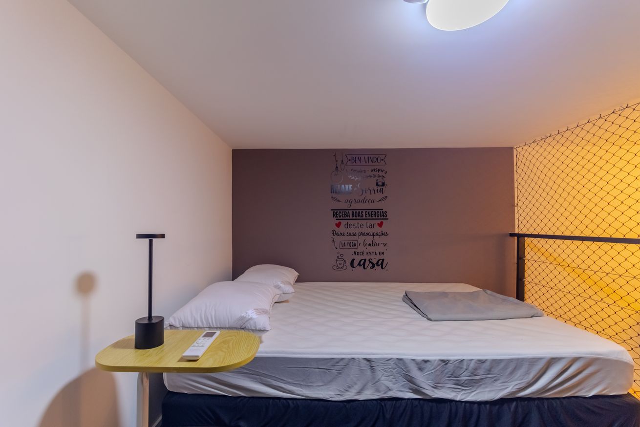 Un lit bien fait, avec une literie blanche, une petite table de chevet avec une lampe et un mur orné de citations inspirantes.