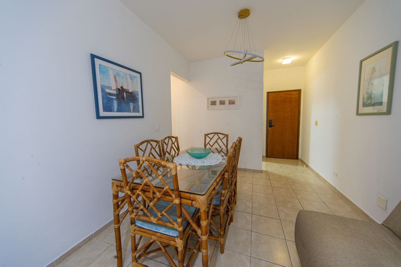 Uma sala de jantar com mesa de vidro, cadeiras de vime e luminária no teto.