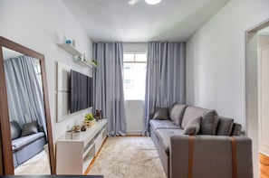 Ein modernes Wohnzimmer mit grauem Sofa, einem an der Wand befestigten Fernseher, einem kleinen weißen Konsolentisch mit Dekoration und einem großen Spiegel.
