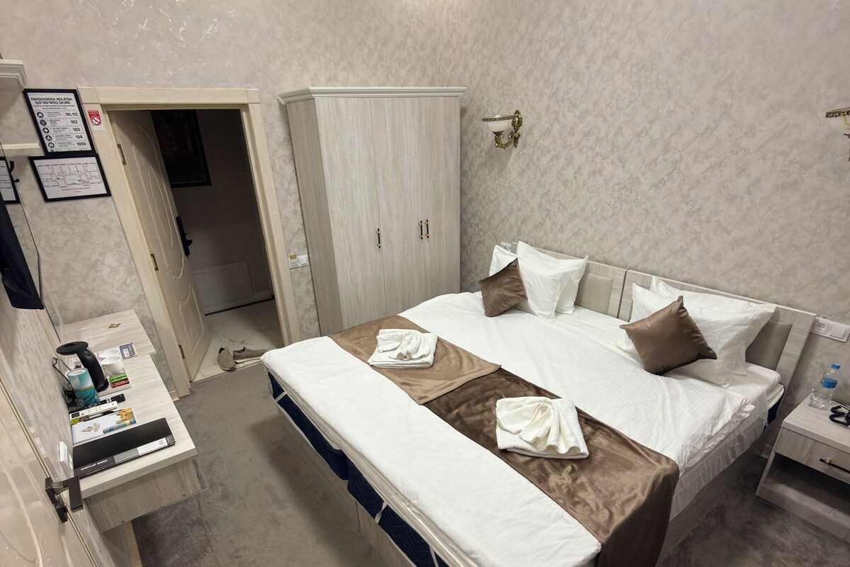 A hotel room with a bed, bedside tables, a wardrobe, and a bathroom.