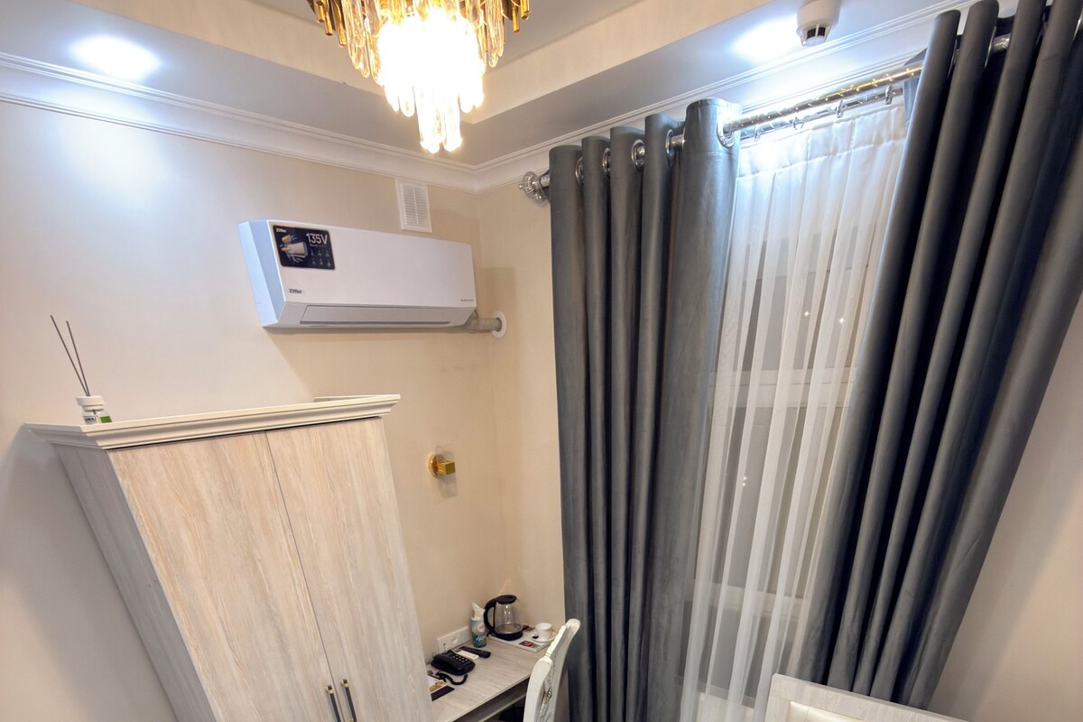 A bedroom with a bed, a desk, a chair, a wardrobe, and an air conditioning unit.
