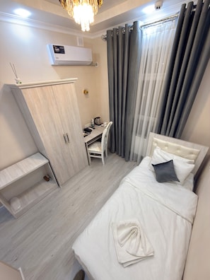 A bedroom with a bed, a desk, a chair, a wardrobe, and an air conditioning unit. - Bekchan Hotel (Xiva)