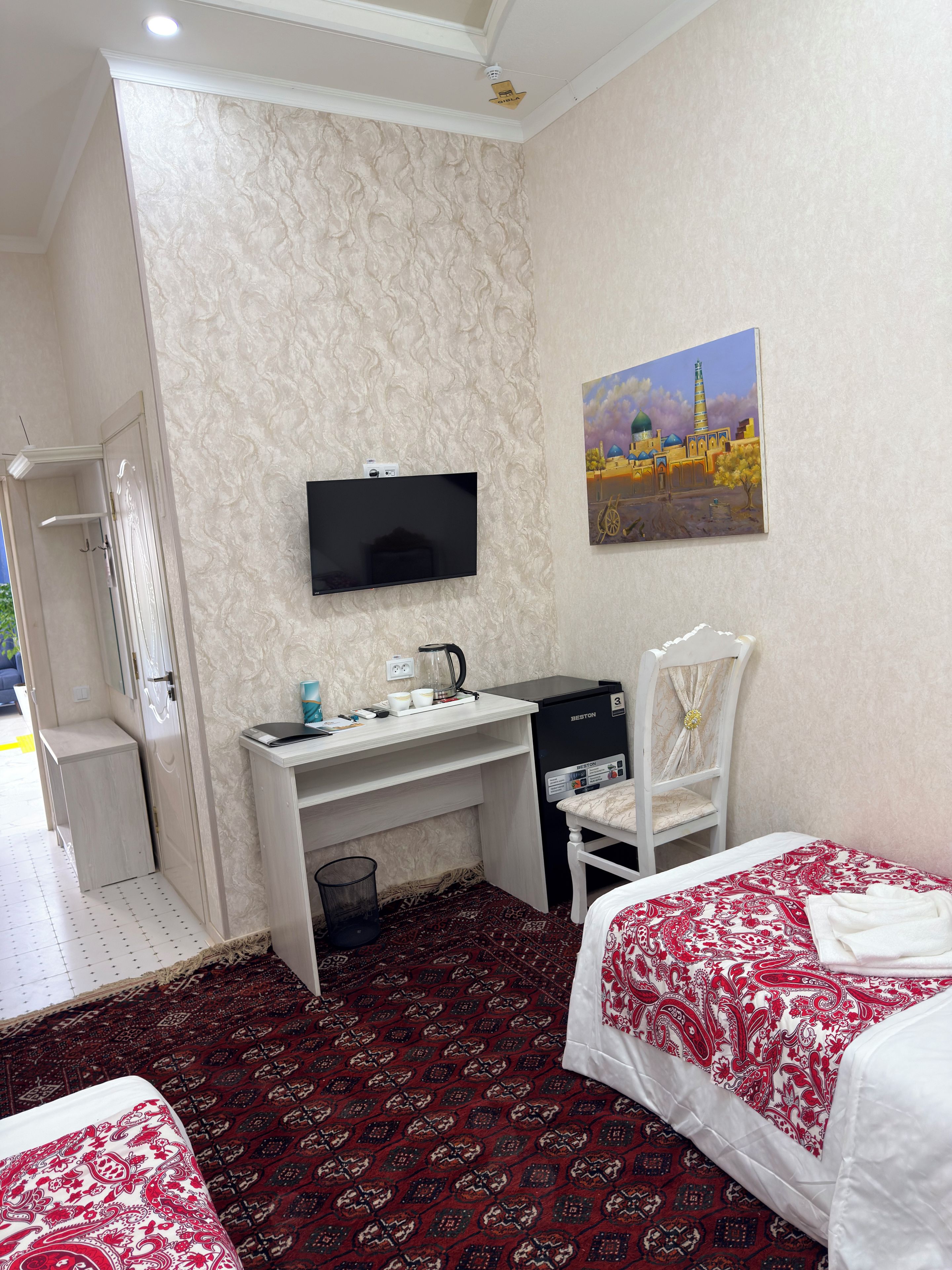 Una habitación de hotel con cama, escritorio, silla, televisor y un cuadro en la pared.