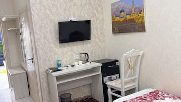A hotel room with a bed, a desk, a chair, a television, and a painting on the wall.