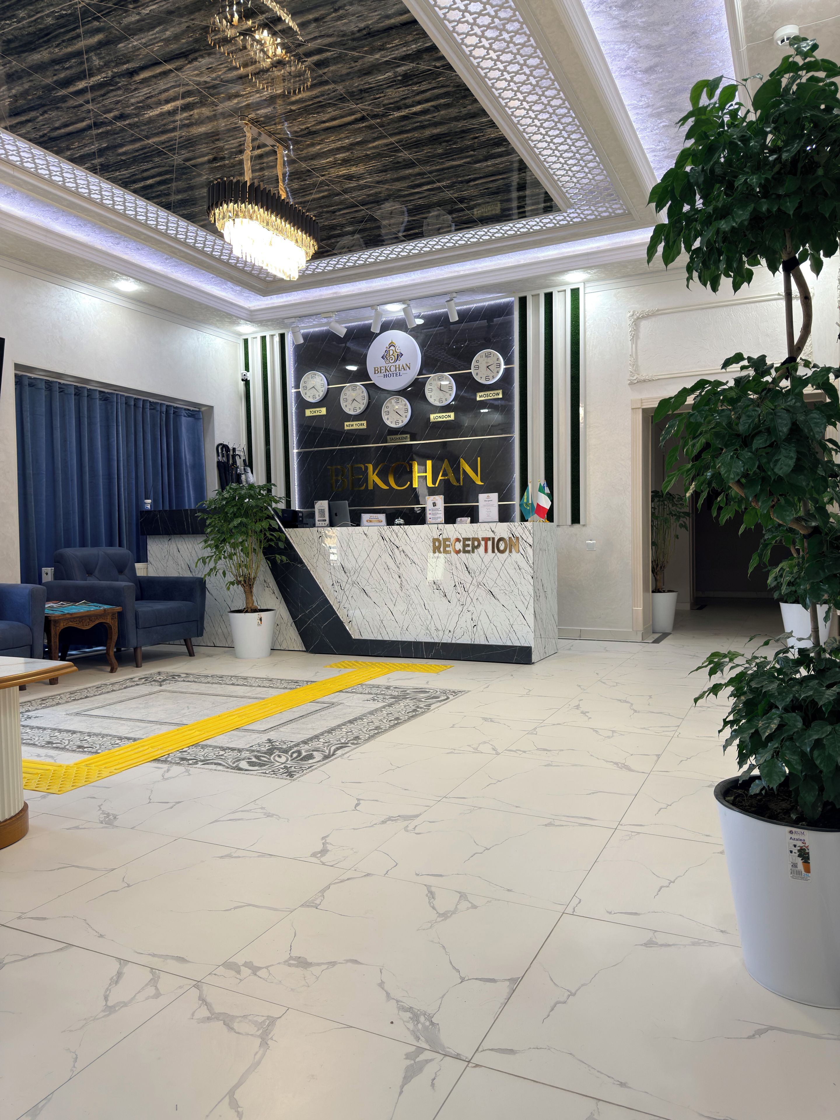 Un hall d’accueil d’hôtel avec un comptoir de réception en marbre, une horloge indiquant plusieurs fuseaux horaires et un panneau indiquant le service de réception.