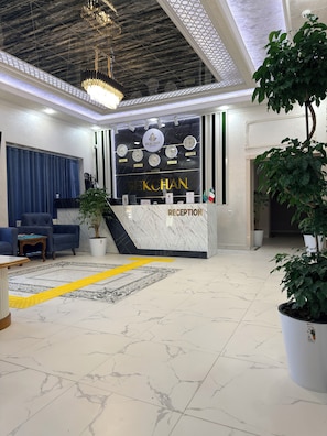 A hotel reception area with a marble reception desk, a clock displaying multiple time zones, and a reception sign. - Bekchan Hotel (Xiva)