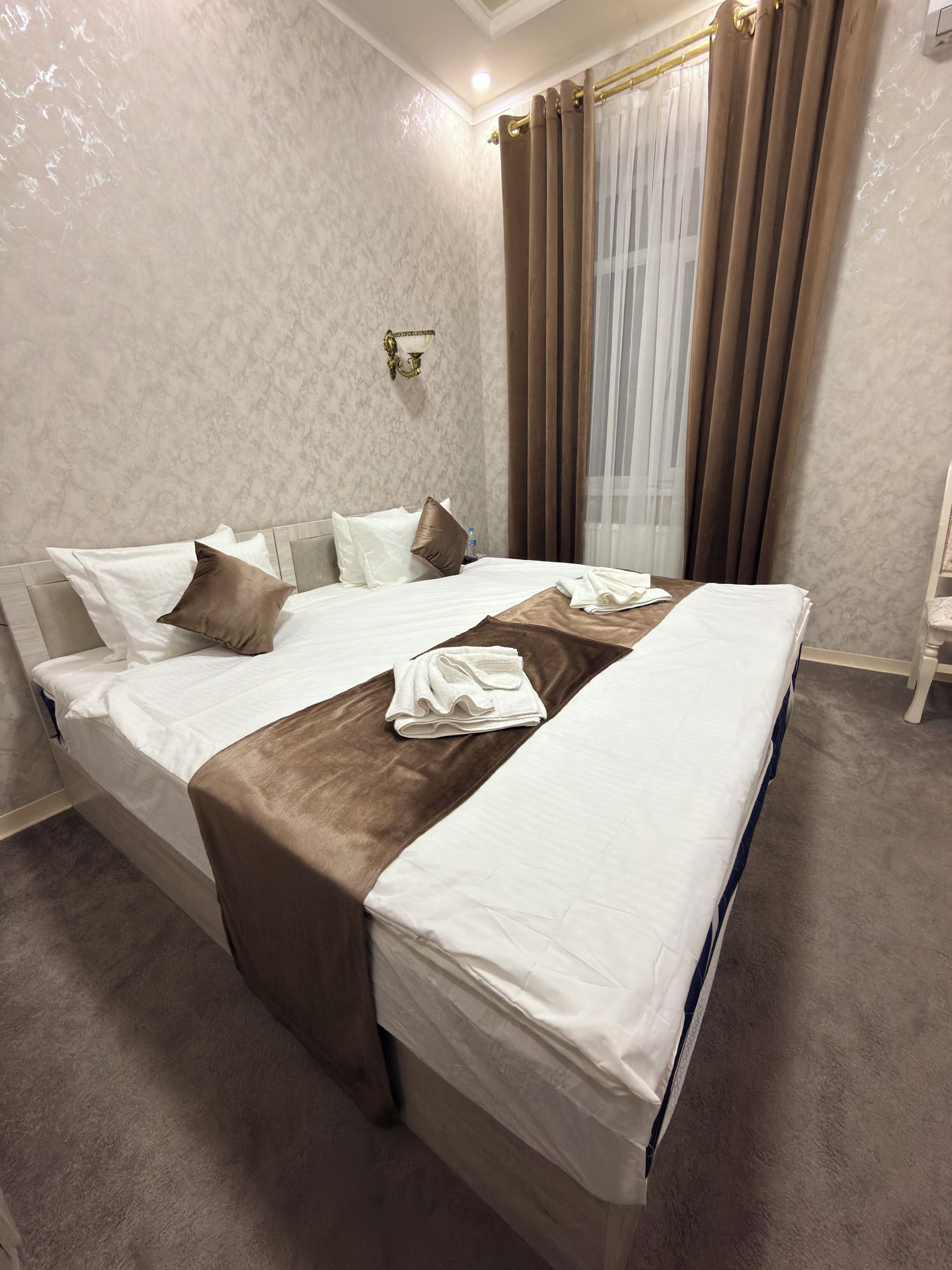 Une chambre d’hôtel avec un grand lit, une table de chevet, un luminaire fixé au mur et une fenêtre avec des rideaux.