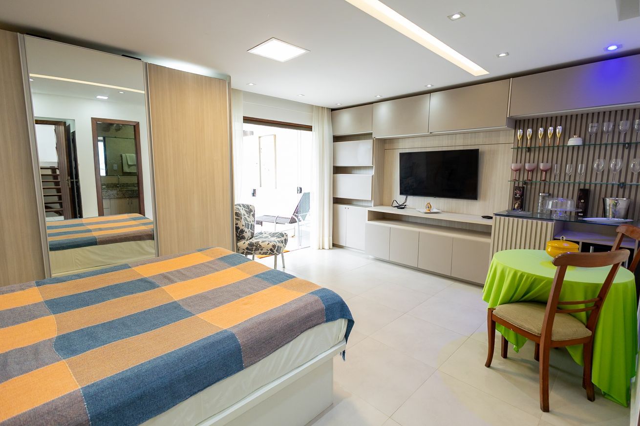 A hotel room with a bed, a TV, a dining area, and a bathroom visible through a mirror.