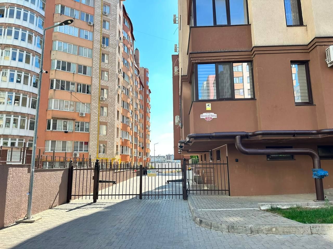 A gated residential area with multi-story buildings, a paved walkway, and a metal fence.