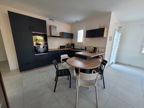 A modern kitchen with black cabinets, a wooden dining table, and four chairs. - New Listing (L'Épine)