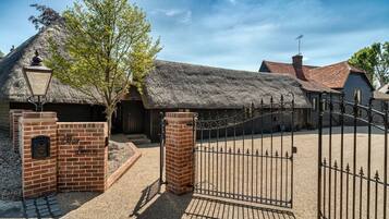 A traditional thatched-roof building with a brick entrance gate and a metal fence.