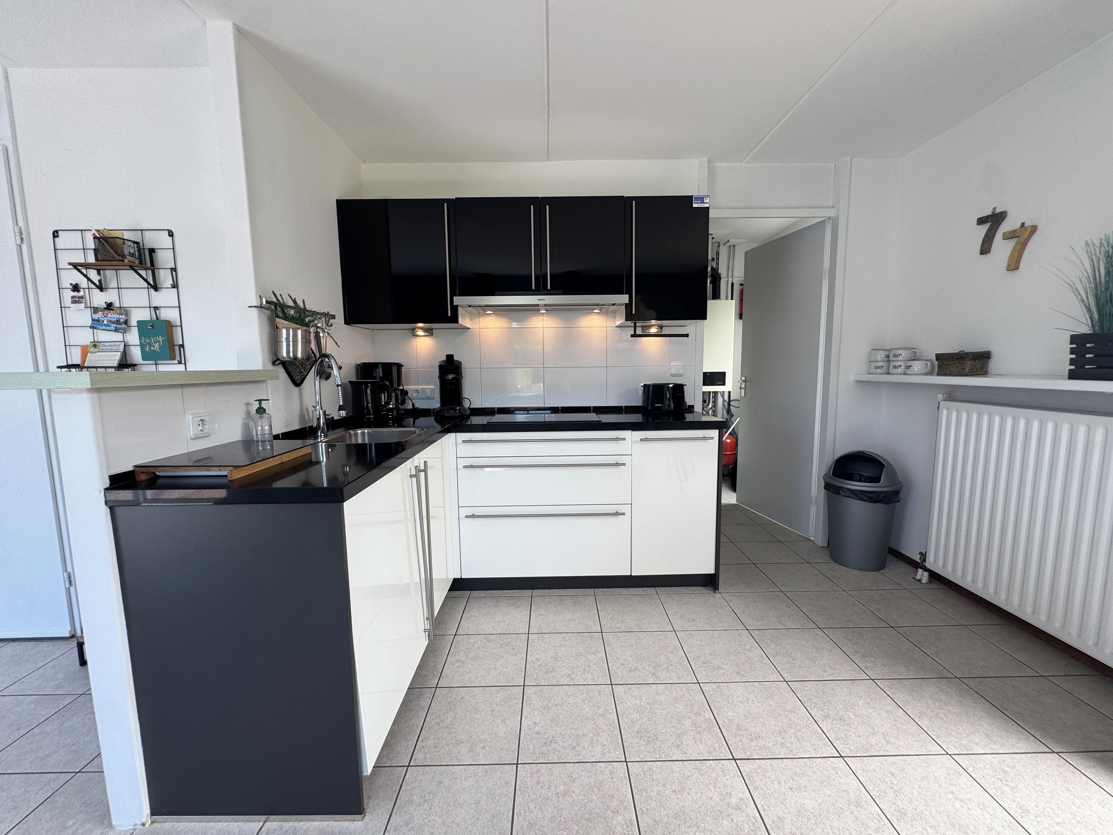 Une cuisine moderne avec des meubles de rangement noirs et blancs, un îlot central et un sol carrelé.