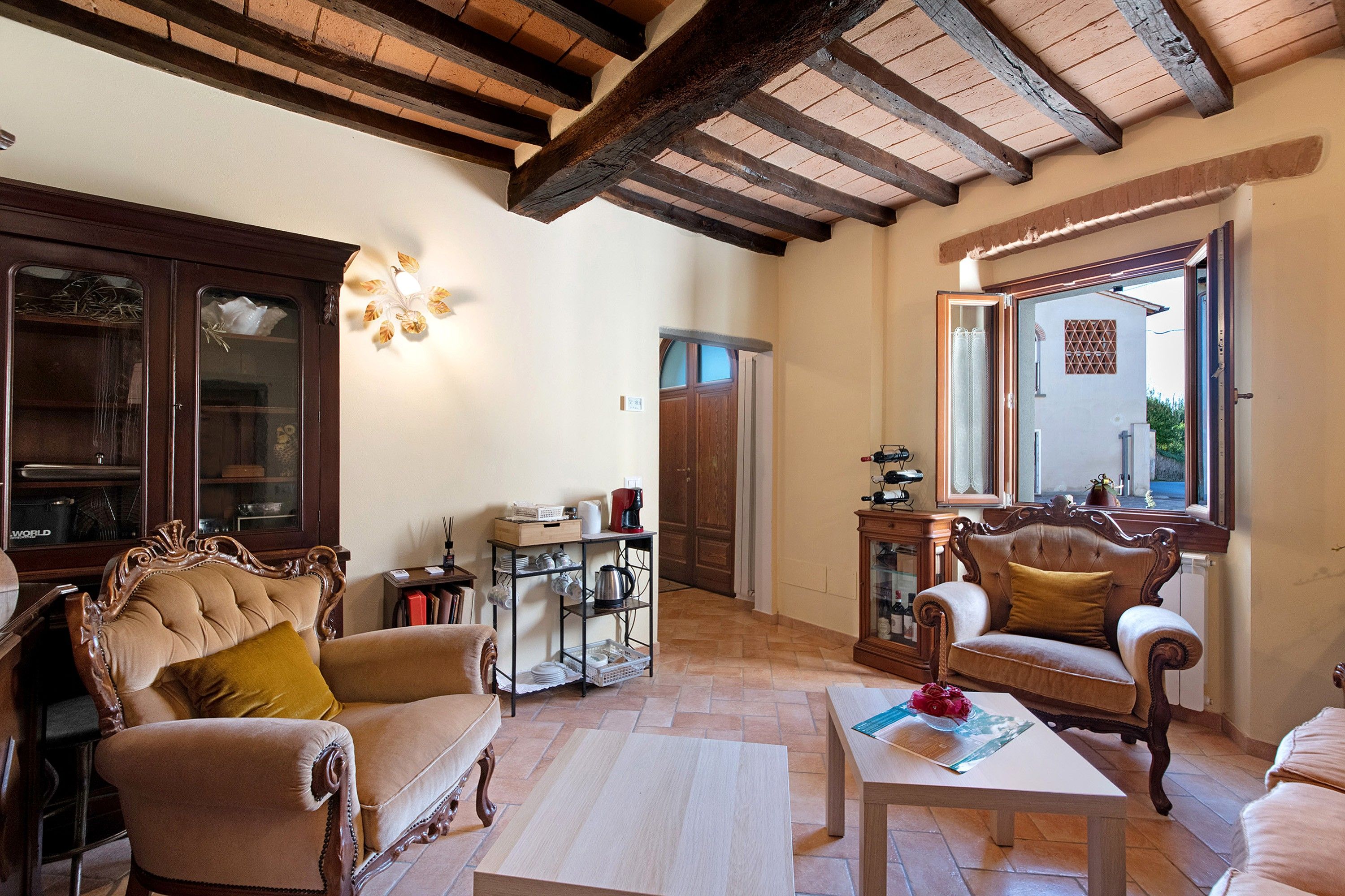 A spacious living room with a high ceiling, wooden beams, and a large window.