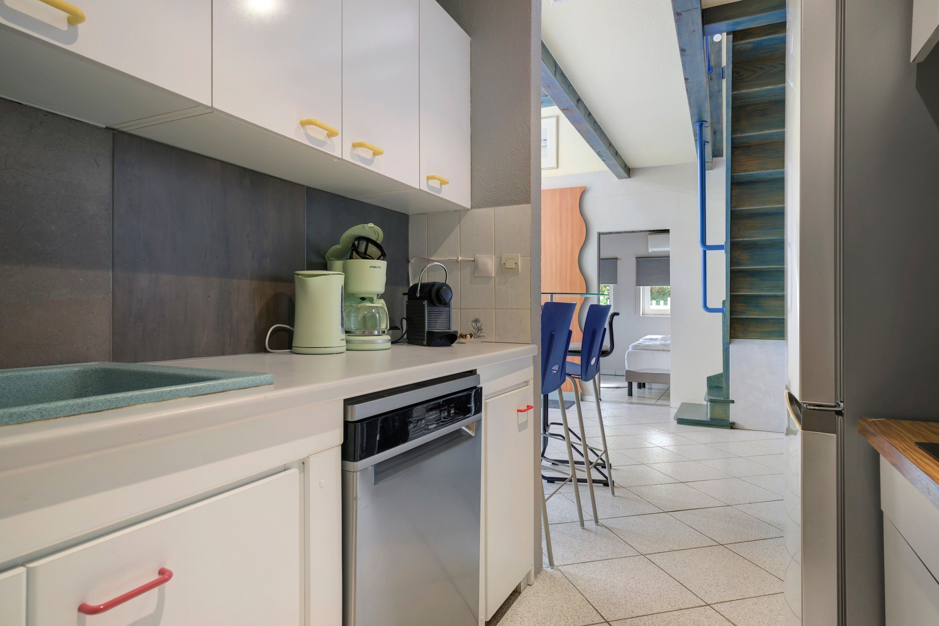 A modern kitchen with white cabinets, a dishwasher, and a coffee maker.