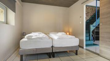 A double bed with white linens in a modern room with a tiled floor and a wooden ceiling.