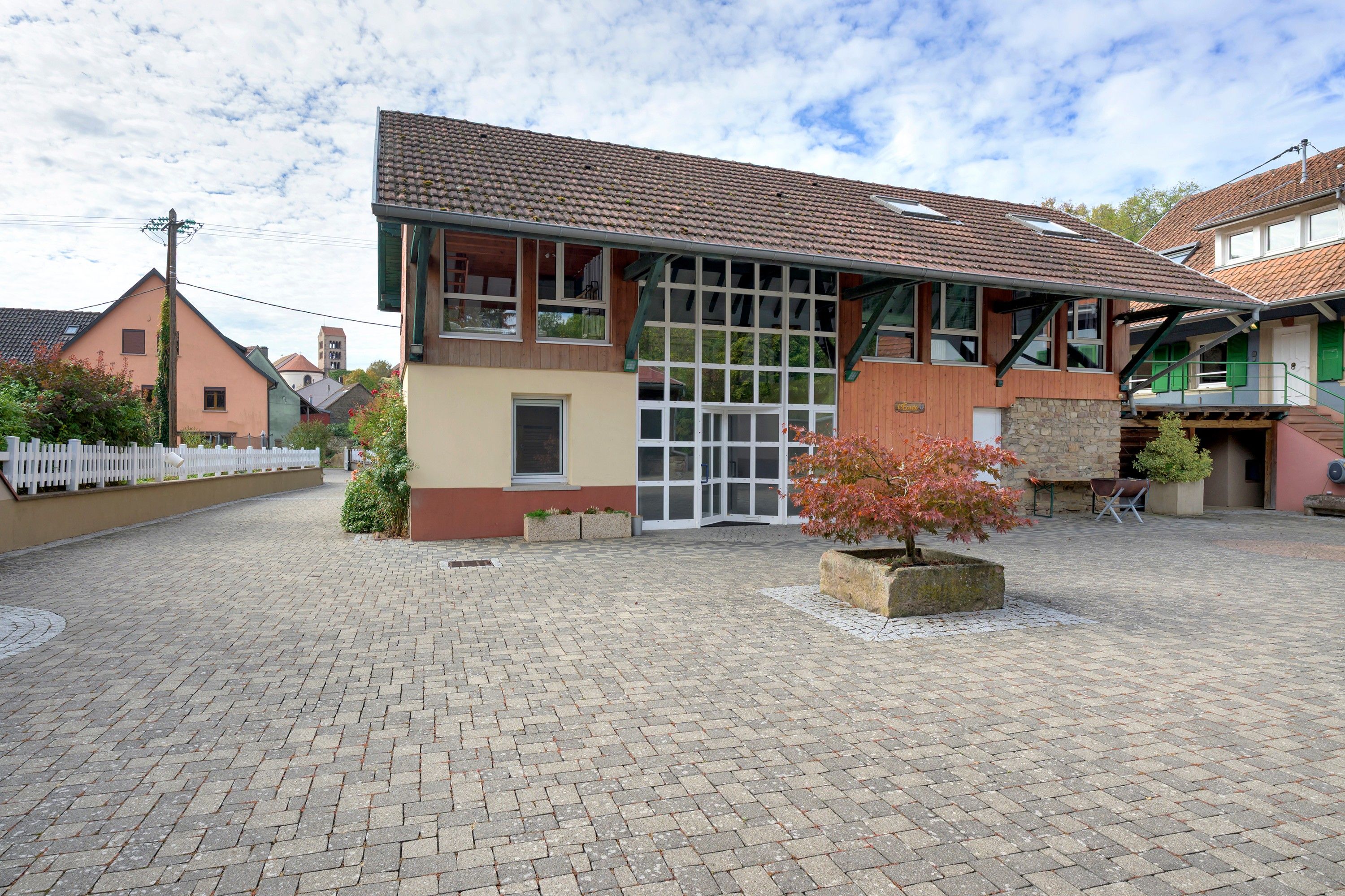 A building with a tiled roof, large windows, and a paved courtyard.