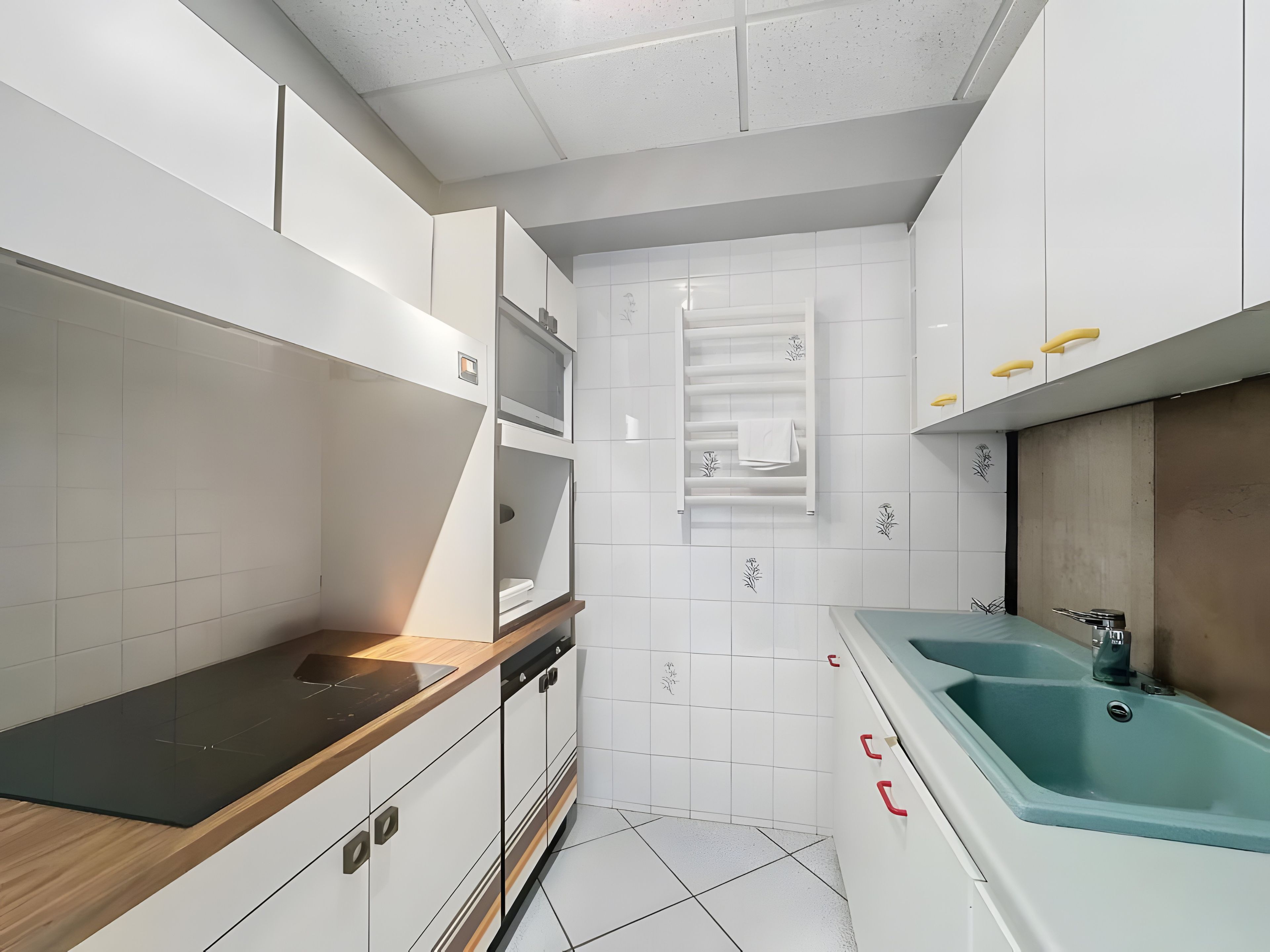 Une cuisine moderne avec des meubles blancs, un plan de travail noir et un évier bleu.
