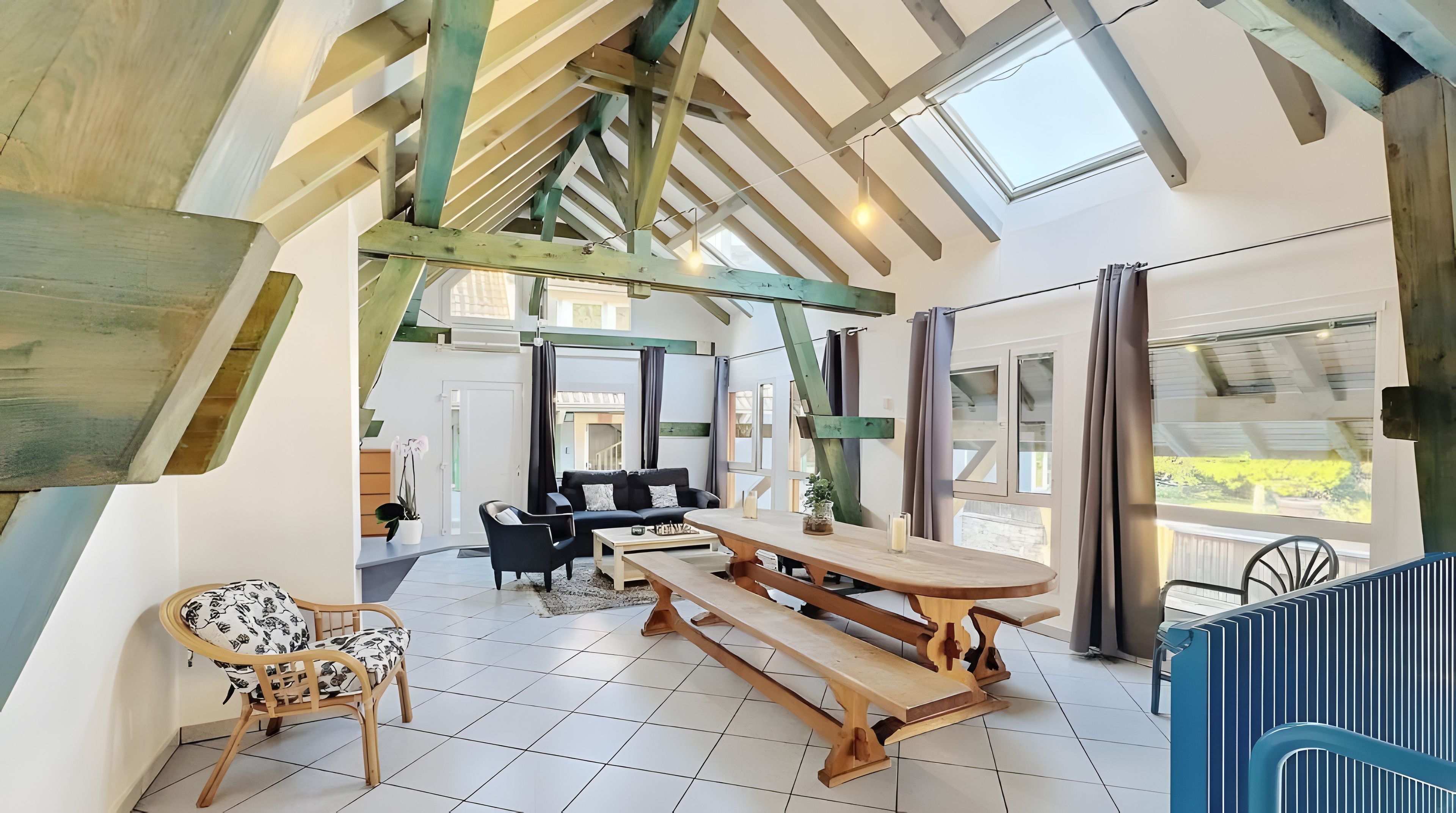 Un loft spacieux avec de hauts plafonds, des poutres apparentes, une grande table à manger et une vue sur l’extérieur.