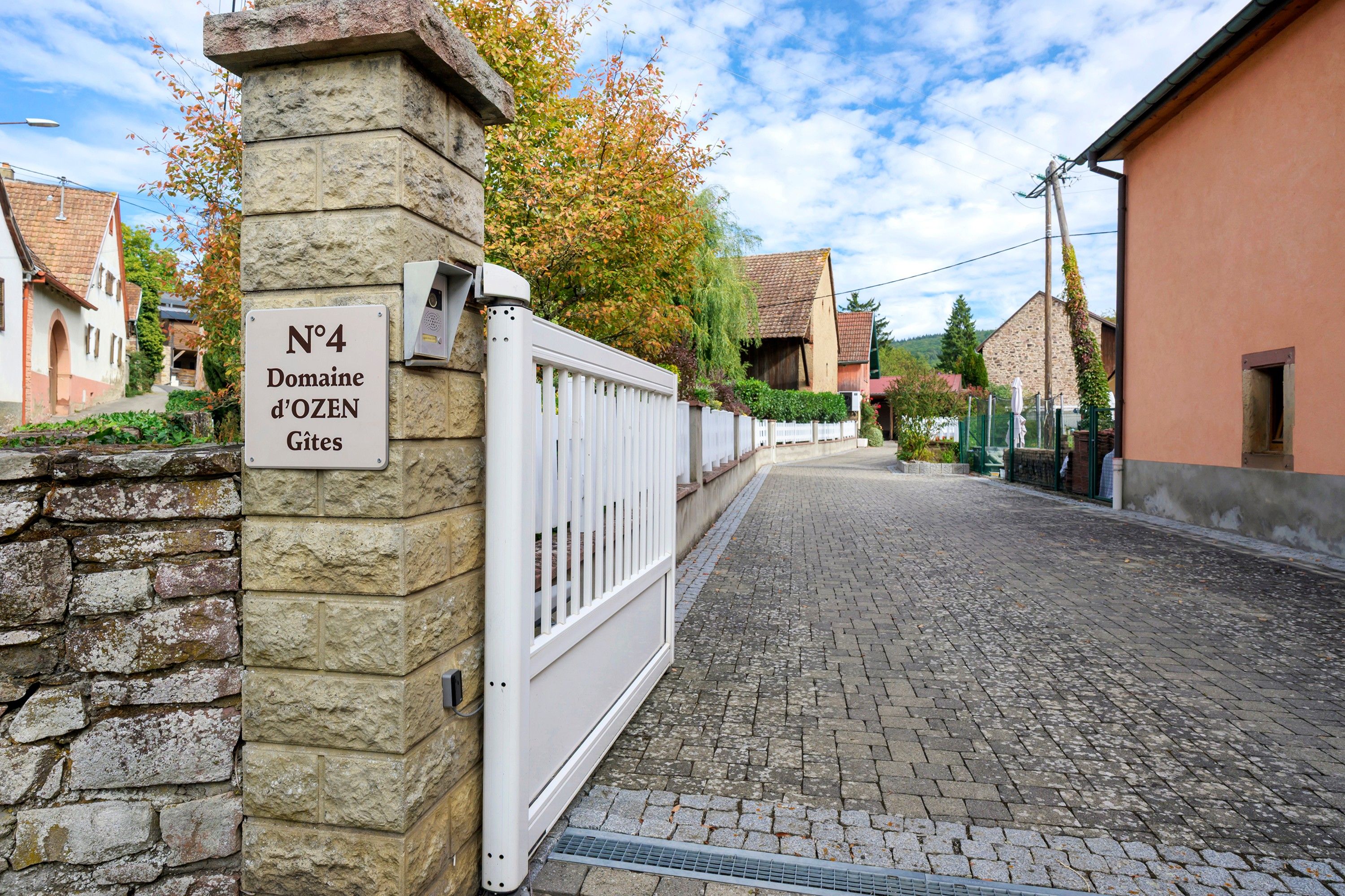 A cobblestone street with a stone wall and a white gate.