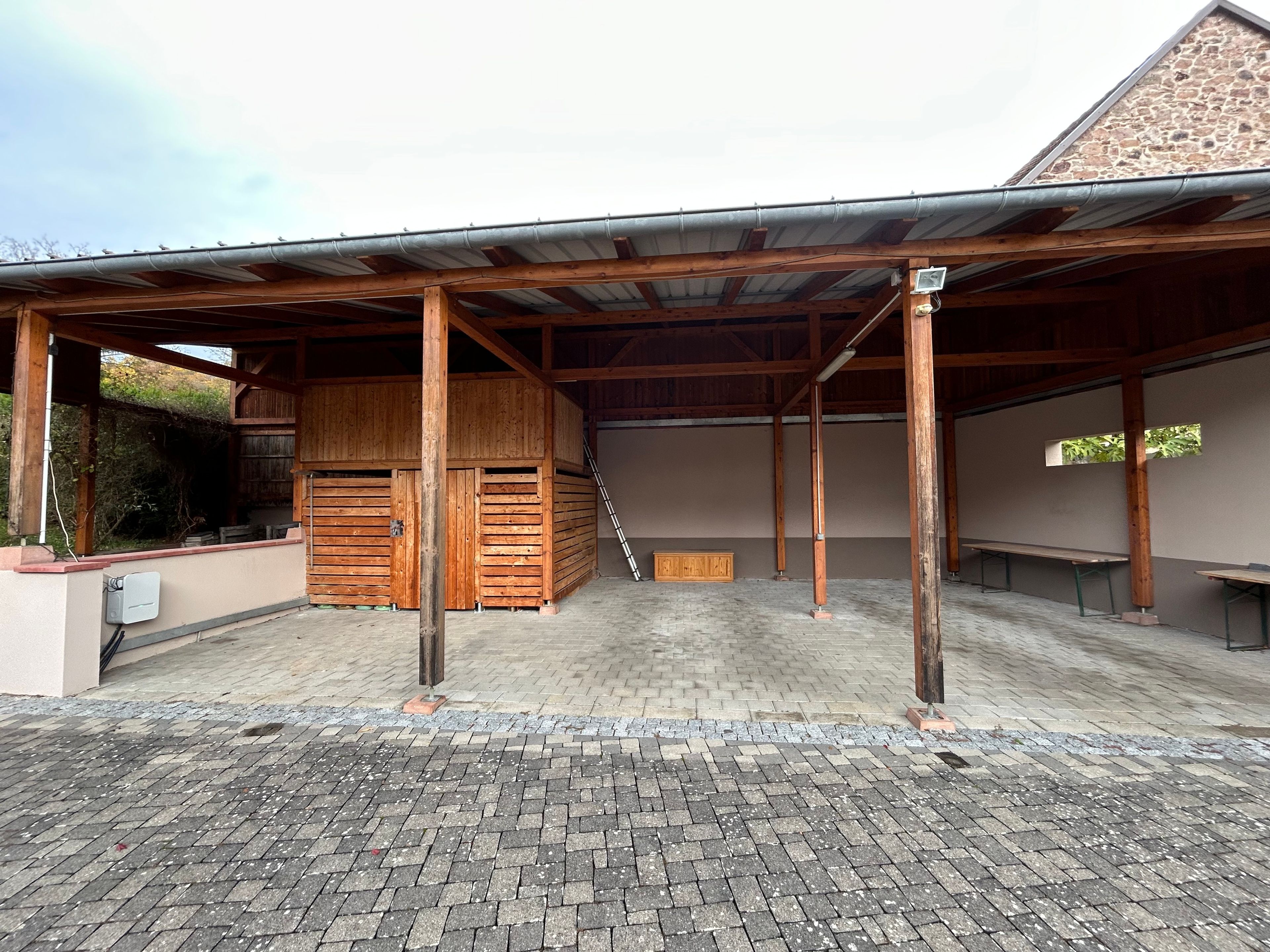 Zona exterior coberta amb sòl de maó, bancs de fusta i teulada metàl·lica.