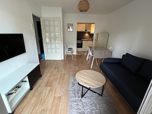 Una sala de estar moderna con un televisor de pantalla plana, un sofá oscuro, una mesa de centro redonda y una zona de comedor con mesa y sillas.
