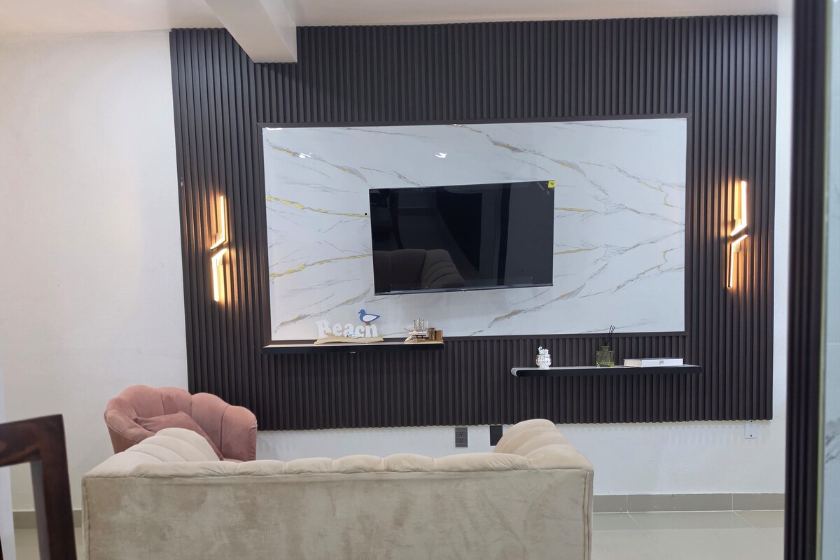 A modern living room with a flat-screen TV mounted on a wall with a marble-like design, a beige sofa, and two wall-mounted light fixtures.