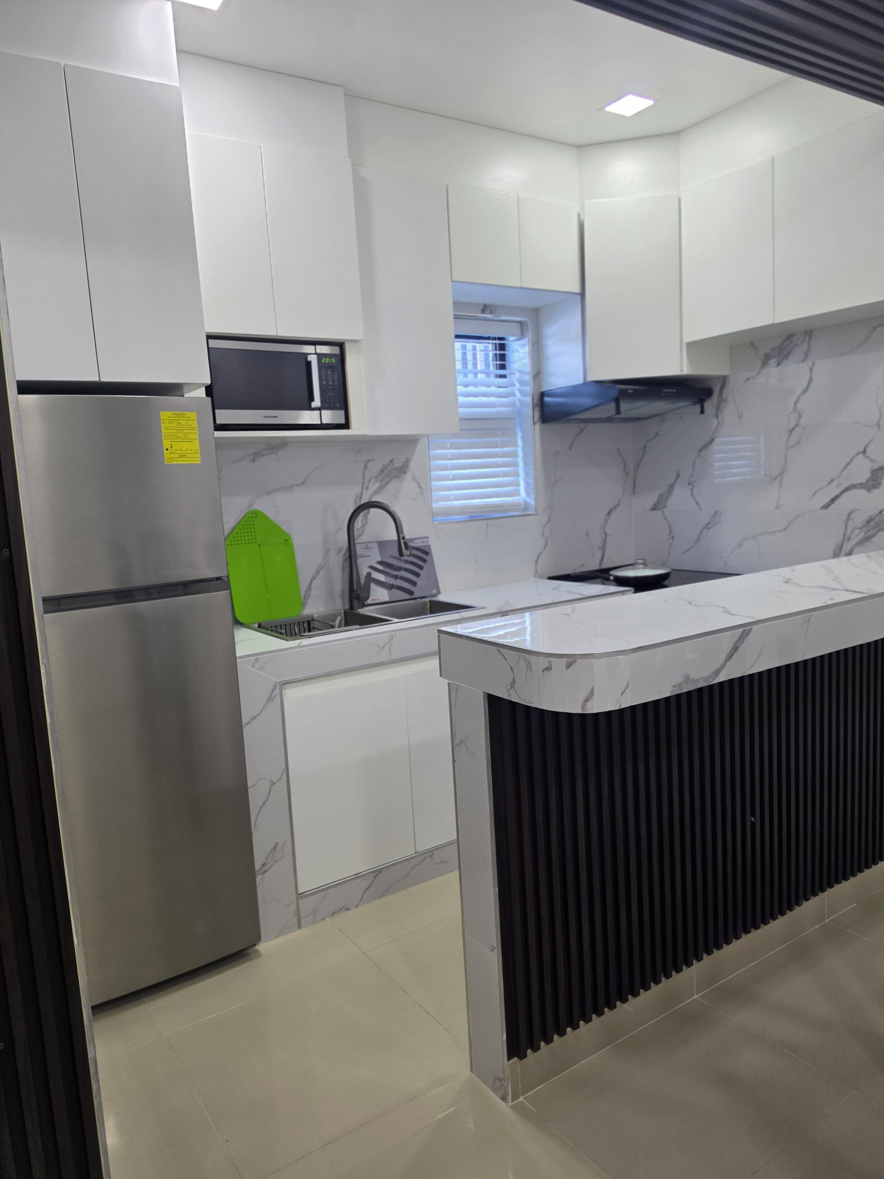 Una cocina moderna con microondas integrado, refrigerador de acero inoxidable y campana extractora negra.