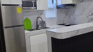 Una cocina moderna con microondas integrado, refrigerador de acero inoxidable y campana extractora negra.