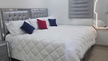 A neatly made bed with a quilted white duvet, a grey upholstered headboard, and a bedside table with a grey cabinet.