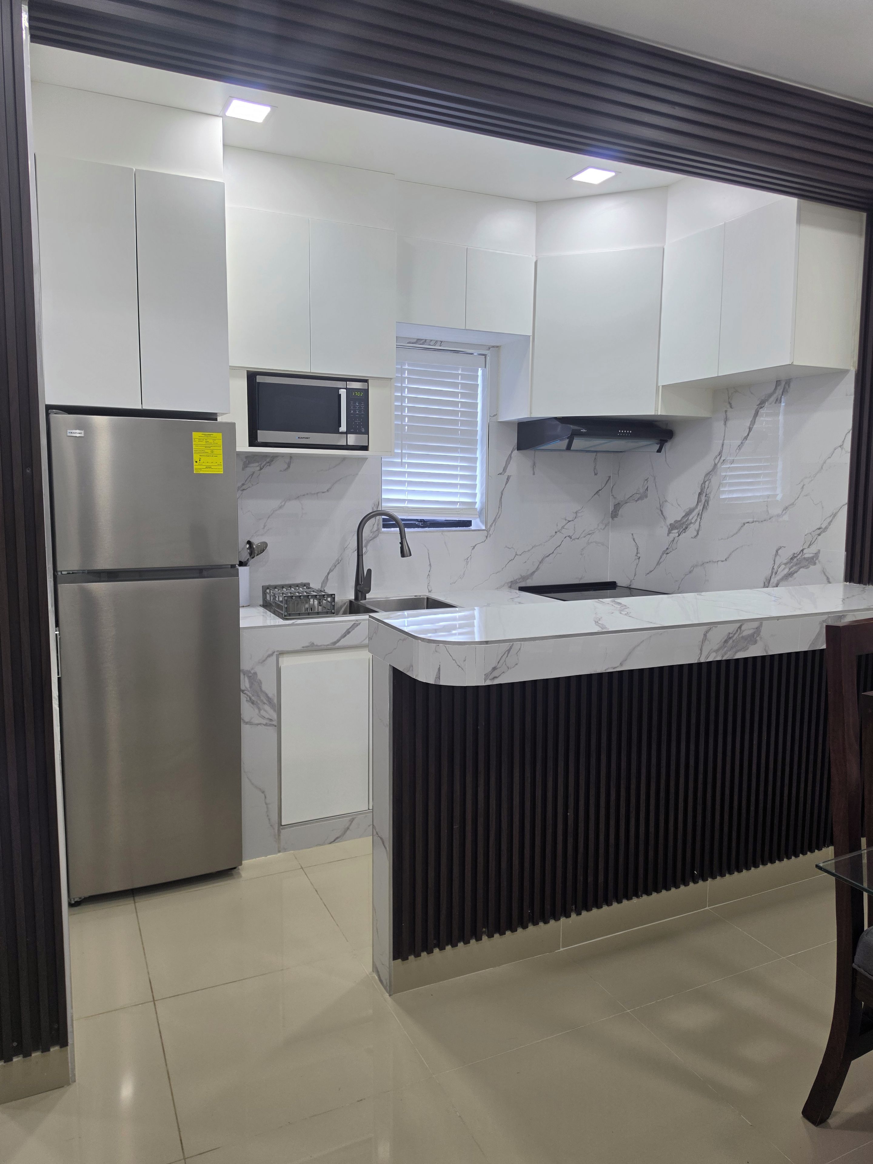 A modern kitchen with a built-in microwave, stainless steel refrigerator, and a marble backsplash.