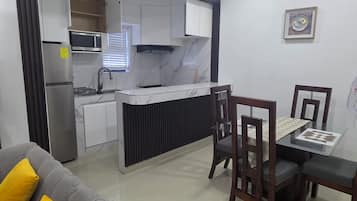 Una cocina moderna con microondas integrado, un comedor con mesa de vidrio y sillas de madera, y un sofá gris con cojines amarillos.