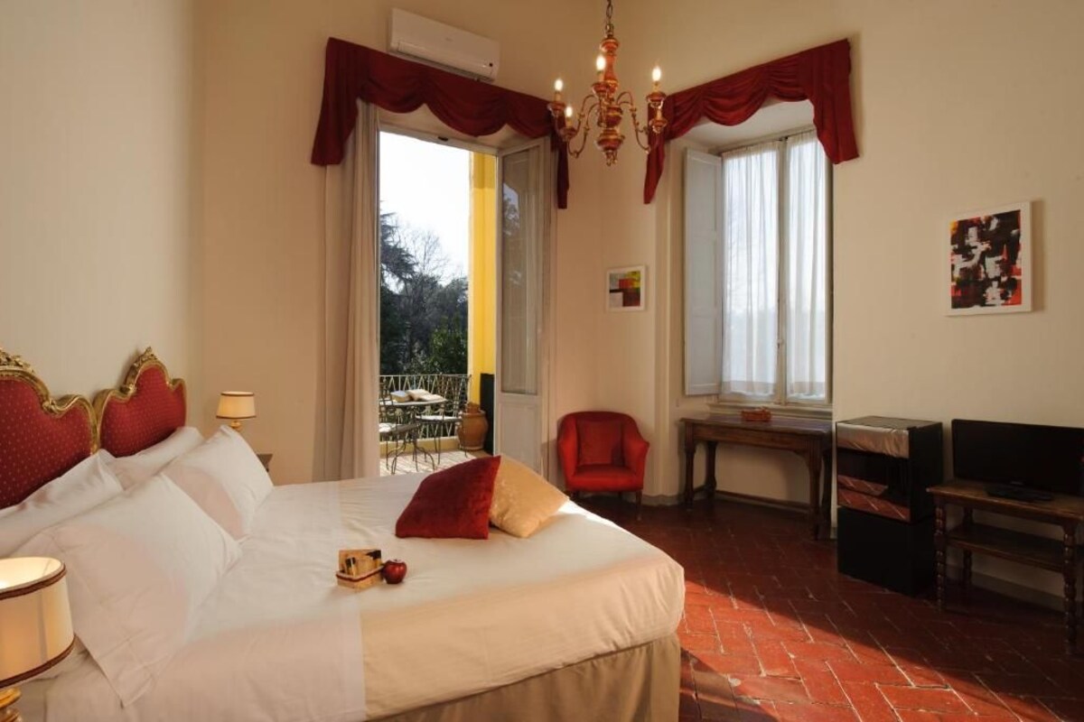 A hotel room with a large bed, a desk, and a chair. There is a balcony with outdoor furniture.