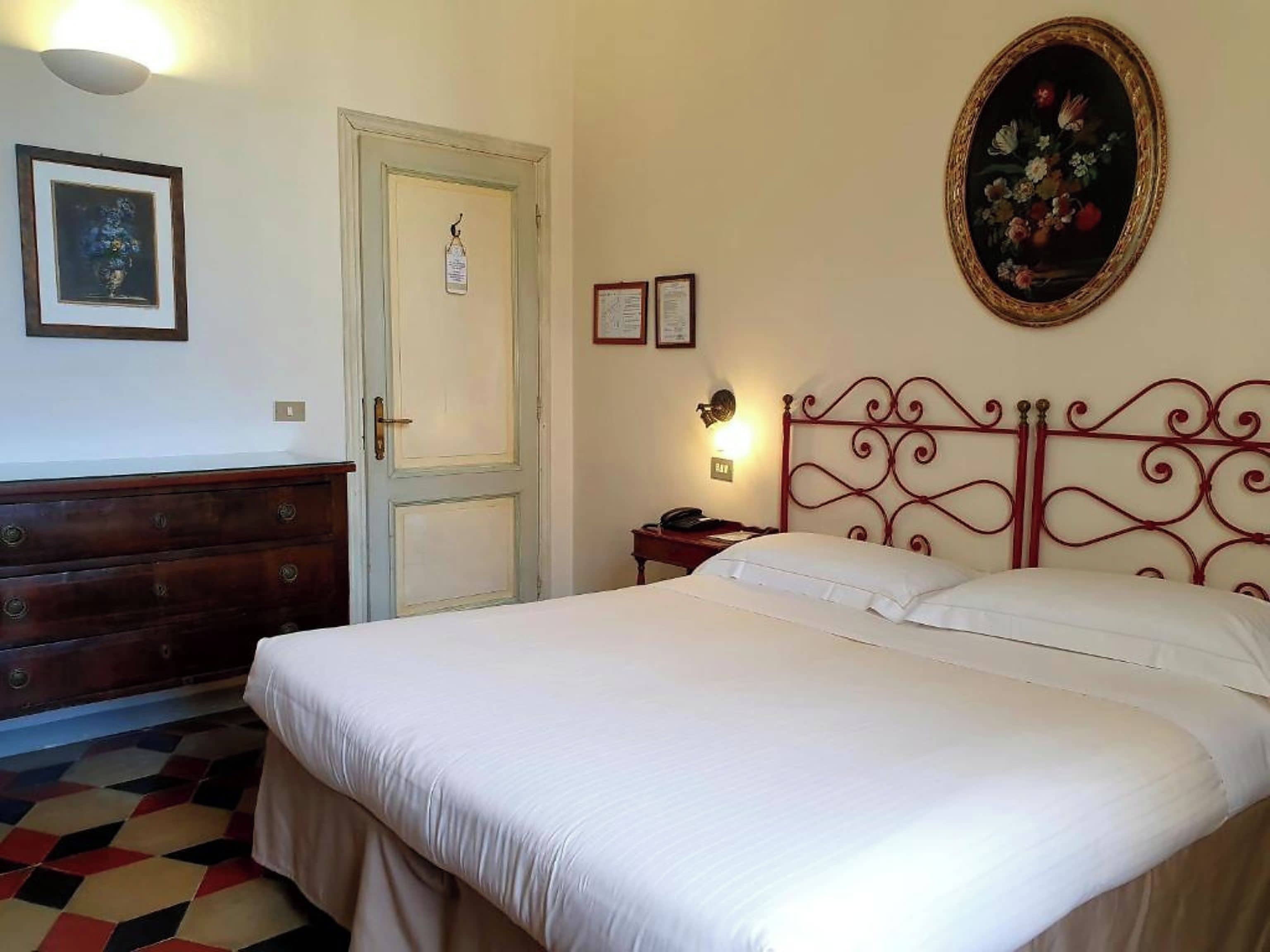 A room with a bed, a dresser, a door, and a wall-mounted lamp.