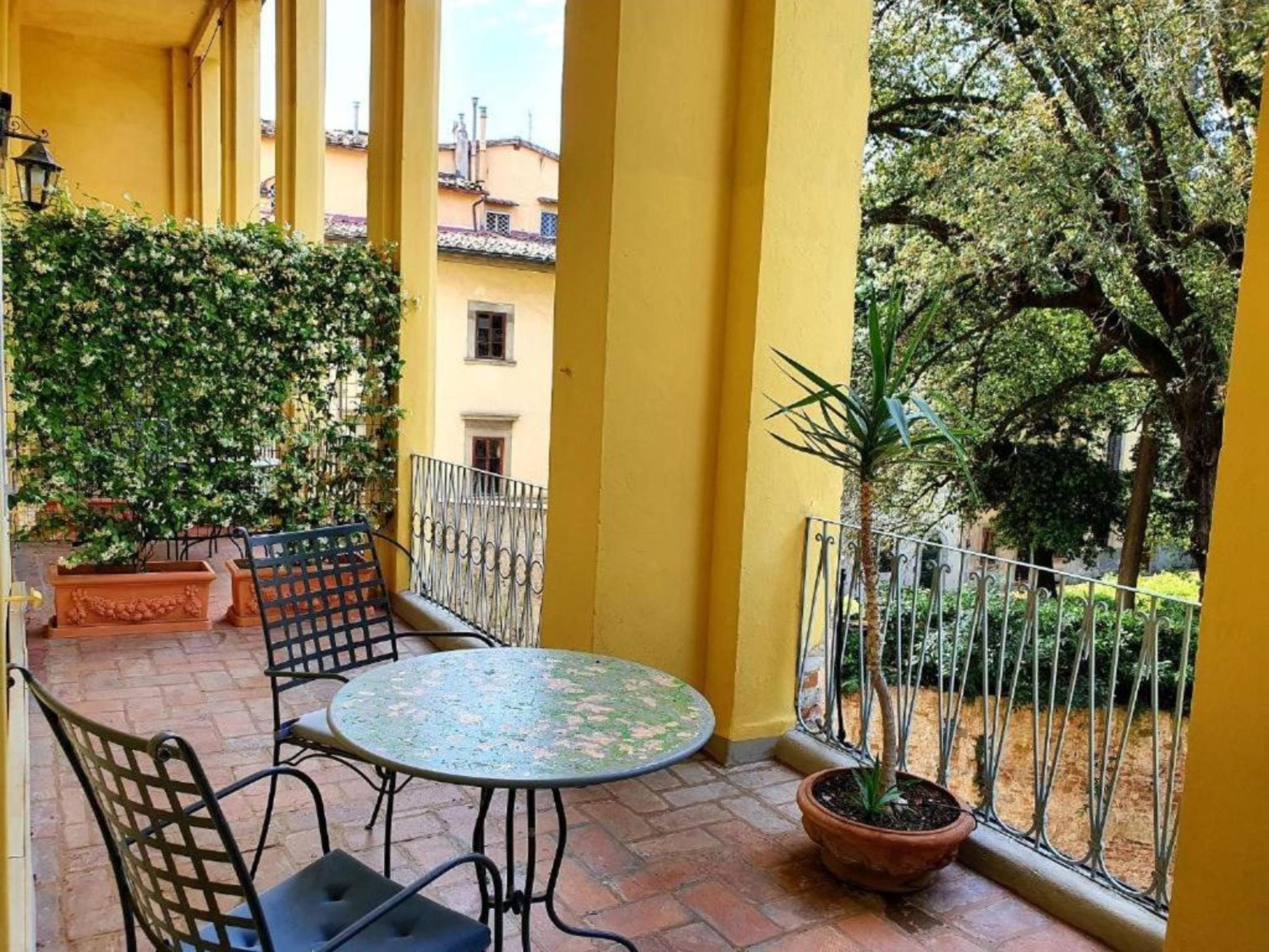 A terrace with a table and chairs, surrounded by yellow walls and potted plants.