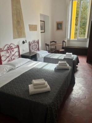 A hotel room with two beds, a small table, and a window with a view of greenery. - Hotel di Annalena (Firenze)