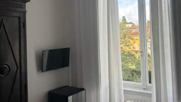 Una habitación con cama, televisor en la pared, radiador y ventana con cortinas.