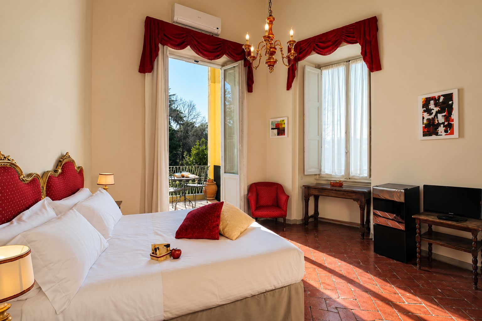 A hotel room with a large bed, a desk, a chair, and a balcony with outdoor furniture.