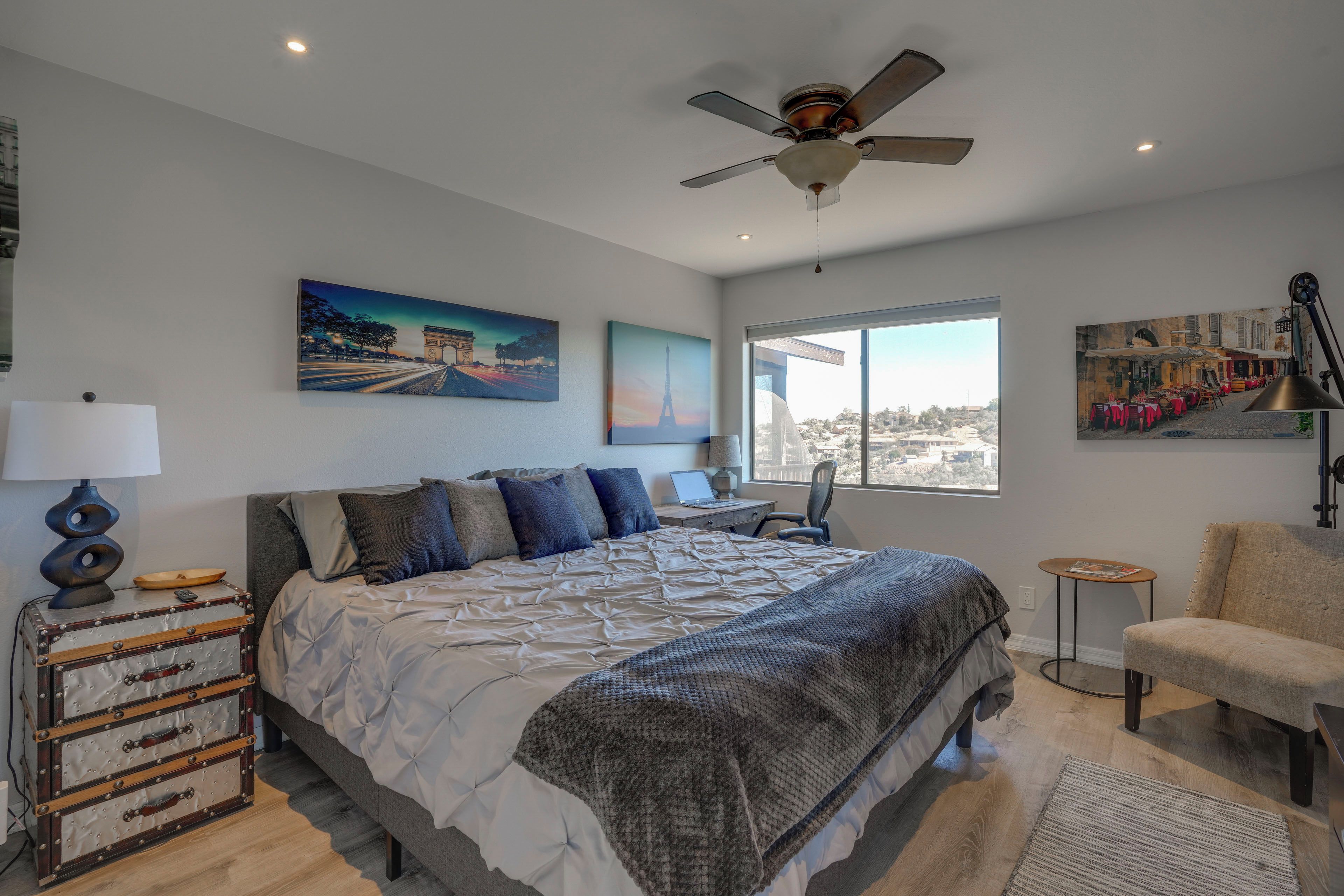 Un dormitorio con cama, escritorio, silla, maleta y ventana con vistas.