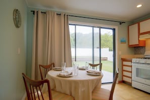 Un comedor con una mesa dispuesta para cuatro, sillas, una ventana con cortinas y una cocina con estufa.