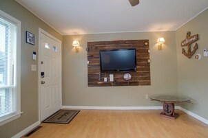 Una sala de estar con un televisor de pantalla plana montado en una pared de madera, una mesa de centro de vidrio y un letrero de bienvenida.