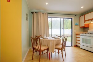 A dining area with a table set for four, chairs, a window with curtains, and a kitchen with an oven.