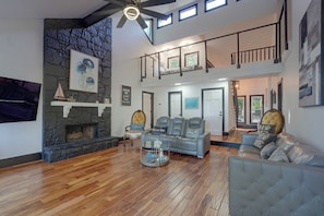 A spacious living area with a stone fireplace, a high ceiling with a fan, and a balcony with railings. - Private Dock! Luxury Beachfront Lake Lanier Escape (Buford)