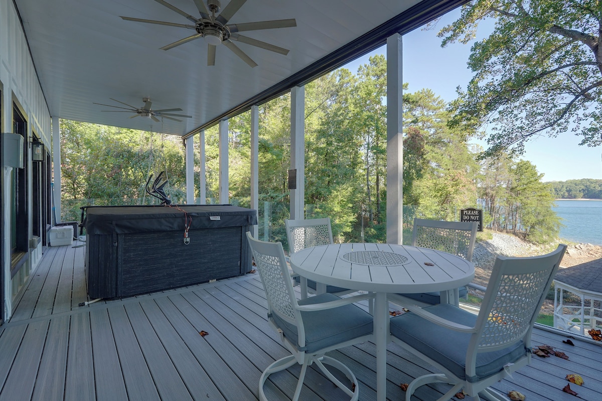 A covered outdoor deck with a round table and chairs, a grill, and a view of a lake.