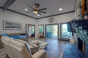 A spacious living room with a ceiling fan, a large painting, a sofa, a coffee table, and a fireplace. - Private Dock! Luxury Beachfront Lake Lanier Escape (Buford)