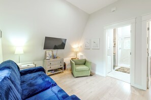 A modern living room with a flat-screen TV, a green armchair, a sofa, and a wooden cabinet.