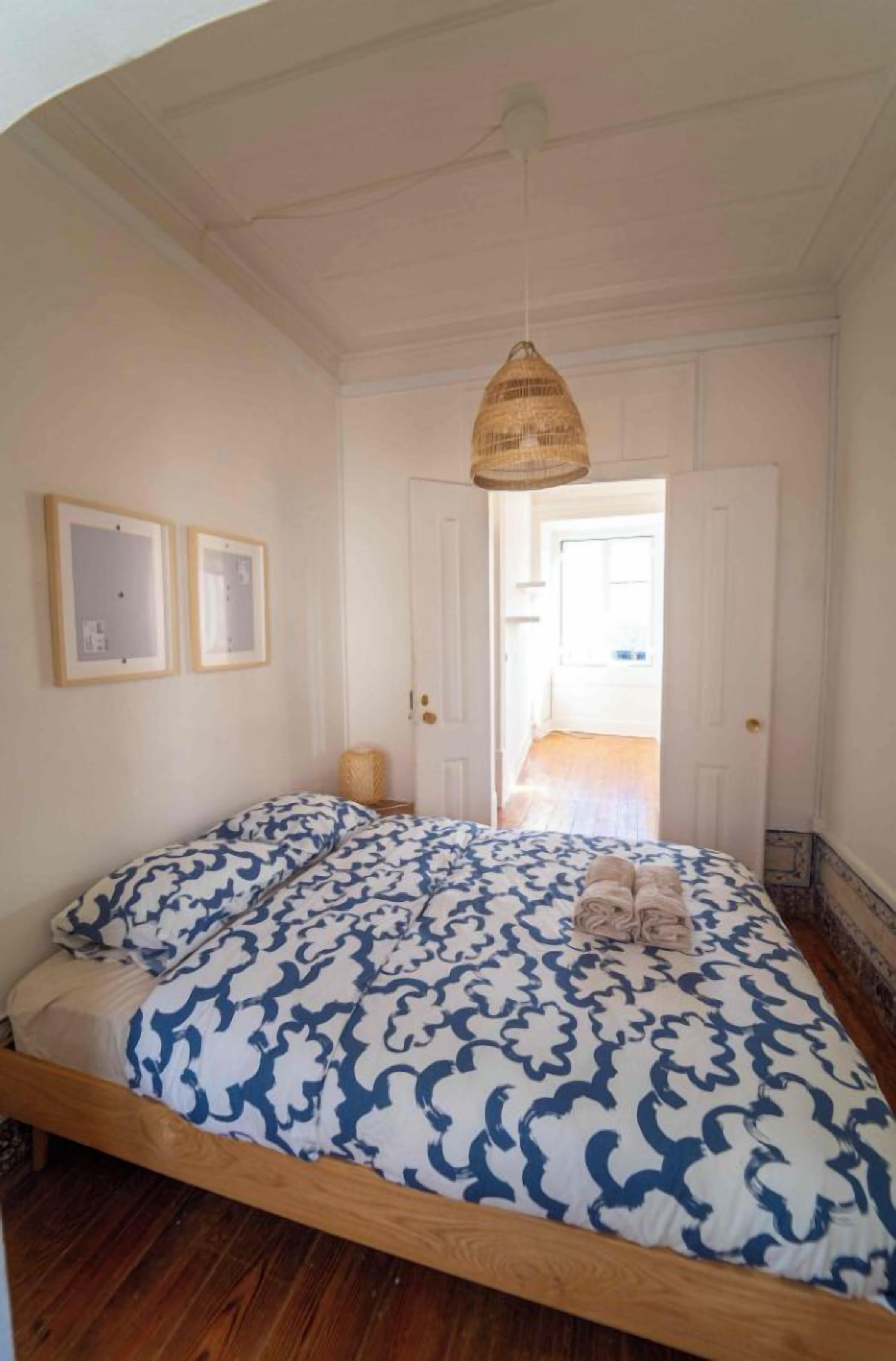 Un dormitorio con cama de madera, lámpara colgante y puerta que da a otra habitación.