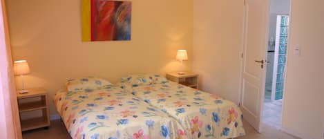 A bedroom with a double bed, two bedside tables, a nightstand, a door to a balcony, and a colorful abstract painting on the wall.